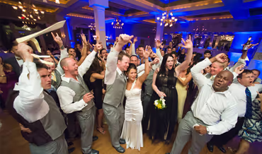 Group of wedding guests and the bride celebrating and dancing joyfully indoors with raised hands and smiles.